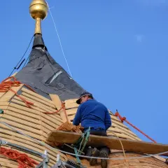 Dekarz pracuje na dachu, montując drewniane łaty pod pokrycie.