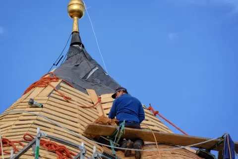 Dekarz pracuje na dachu, montując drewniane łaty pod pokrycie.